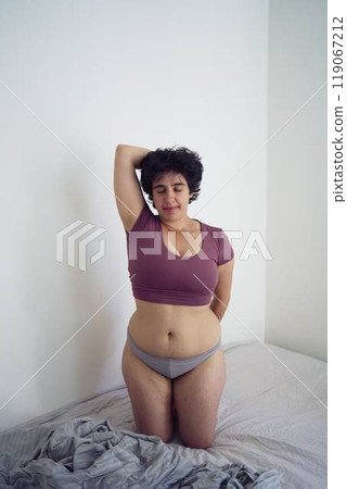 playful young plus size woman in home clothes on bed in student dormitory 119067212