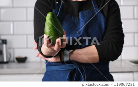 Girl In Apron Showing Raw Green Avocado In Kitchen Girl In Apron Showing Raw Green Avocado In Kitchen 119067281