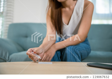 Close up woman hands using rapid antigen test kit for selftest, female four drops of liquid to perform fast coronavirus ATK self test at home in living room on sofa after lockdown and Home Isolation 119067632