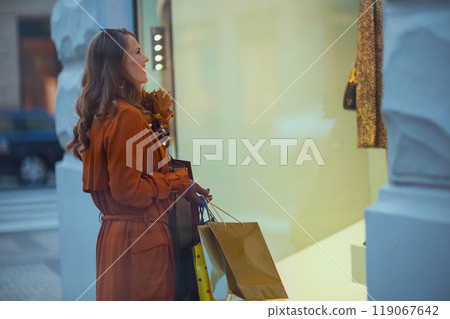 smiling trendy woman in brown trench coat with shopping bags 119067642