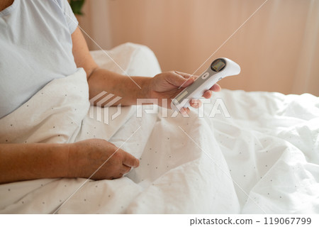 Illness tired Caucasian 50s senior woman touching forehead after using thermometer to checking body temperature and take medicine lying under blanket on bed. Sick female with cold lying in bed with Illness tired Caucasian 50s senior woman touching forehead after using thermometer to checking body temperature and take medicine lying under blanket on bed. Sick female with cold lying in bed with 119067799