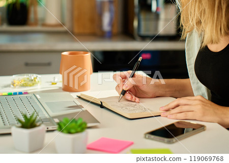 Person is sketching in notebook while working remotely at desk with laptop. Freelance work at home office. Graphic designer drawing sketch 119069768