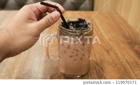 Ice milk cincau is a traditional cold beverage from Indonesia or iced grass jelly with milk and brown sugar. A hand holding a straw. 119070171