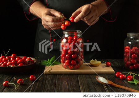 Adding ripe cherries to a jar by the chef hands. The concept of making a delicious sweet cherry compote 119070940