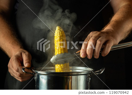 Chef takes hot head of corn from pan with tongs. Concept of cooking maize in kitchen. Corn food for lunch 119070942