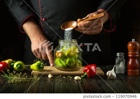 Chef adding salt to a jar of pickled pepper. Concept of making a delicious marinade for peppers with spices and garlic 119070946