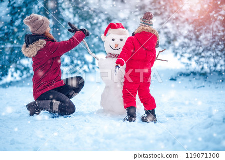 Mother and her son making snowmen in natural park. 119071300