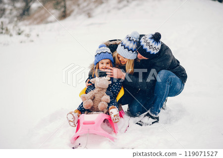 Family have fun in a winter park. Stylish mother in a blue jacket. Little girl on a pink sled. Father with cute daughter Family have fun in a winter park. Stylish mother in a blue jacket. Little girl on a pink sled. Father with cute daughter 119071527