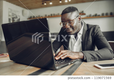 African man. Guy in a black suit. Male with a laptop. Businessman at the office. 119071569