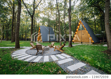 Modern wooden A-frame cabins in forest with outdoor seating and fire pit area, relaxation time 119072039