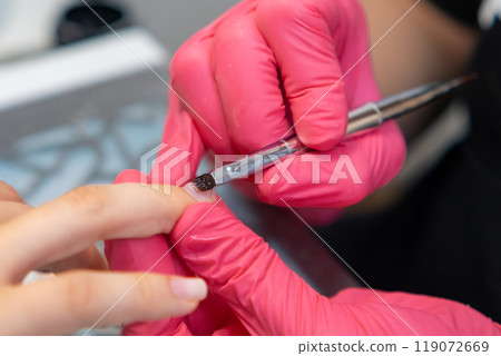 Professional nail technician applying base coat and gel polish using a brush during a manicure session. 119072669