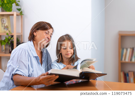 Girl going through book with grandmother on table Girl going through book with grandmother on table 119073475