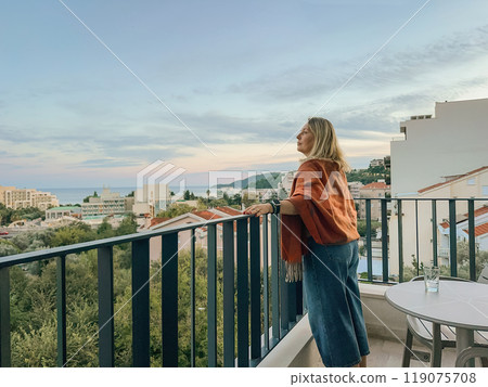 A woman standing on the balcony at summer sunset 119075708