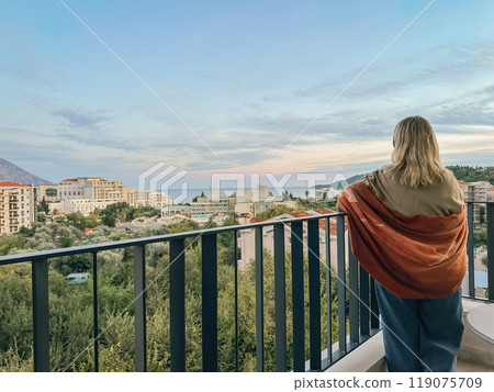 A woman standing on the balcony at summer sunset 119075709