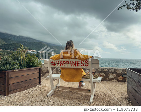A woman in a yellow raincoat sits on a bench 119075738