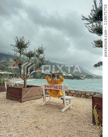 A woman in a yellow raincoat sits on a bench 119075758