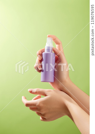 The image is perfect for promoting skincare items since a hand tenderly administers a purple spray lotion to the skin, showing its moisturizing qualities against a green backdrop. 119076595