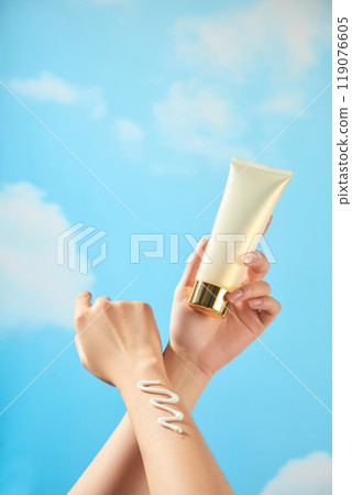 The model hands rub together, squeezing a zigzag cream streak and holding a beige tube cream mockup with a copper gold cap in a blue summer scene for sunscreen advertising photo templates. The model hands rub together, squeezing a zigzag cream streak and holding a beige tube cream mockup with a copper gold cap in a blue summer scene for sunscreen advertising photo templates. 119076605