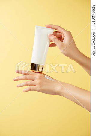An unmarked white tube containing white cream is applied by hand to the palm of the hand, evoking the essence of a skincare routine in a warm, yellow-toned setting ideal for advertisements. 119076628