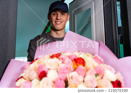 delivery guy with a beautiful bouquet of multi-colored roses and a smile on his face at the door, close-up 119078390