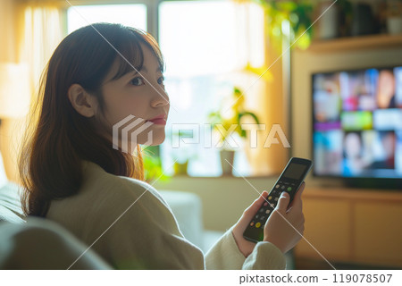 Young Asian woman holding a TV remote control Young Asian woman holding a TV remote control 119078507