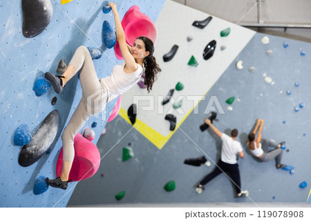 Motivated young girl climbing without ropes and harnesses on artificial bouldering wall in fitness center 119078908