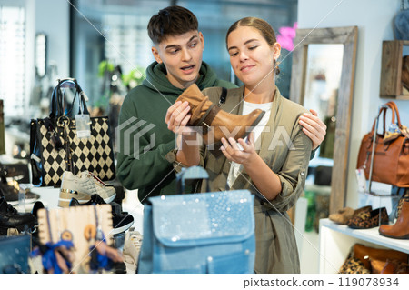 Young guy and girl choosing demi-season womens boots in shoe store Young guy and girl choosing demi-season womens boots in shoe store 119078934