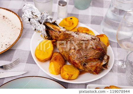 Traditional Spanish lunch is served - fried baked leg of lamb with side dish of potatoes 119078944