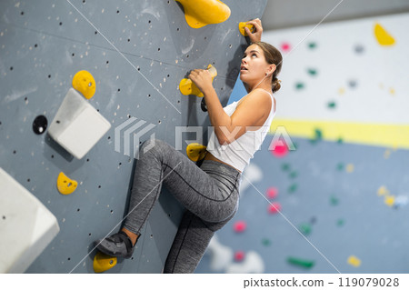 Sportive woman climbing on artificial rock wall in rock climbing gym Sportive woman climbing on artificial rock wall in rock climbing gym 119079028