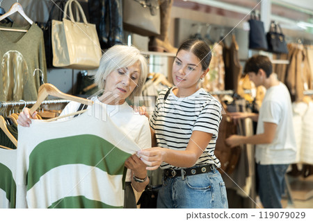 Young girl consults senior female friend about purchasing sweater during shopping 119079029