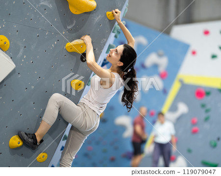 Motivated young girl climbing without ropes and harnesses on artificial bouldering wall in fitness center Motivated young girl climbing without ropes and harnesses on artificial bouldering wall in fitness center 119079047