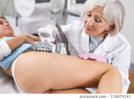 Young woman getting ultrasound cavitation body contouring treatment, anti-cellulite therapy, vacuum massage from old female cosmetologist. Hardware cosmetology for body sculpting 119079141