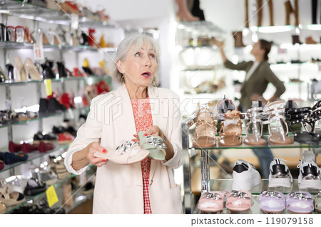 Mature woman who came to shoe store for shopping, chooses summer shoes Mature woman who came to shoe store for shopping, chooses summer shoes 119079158