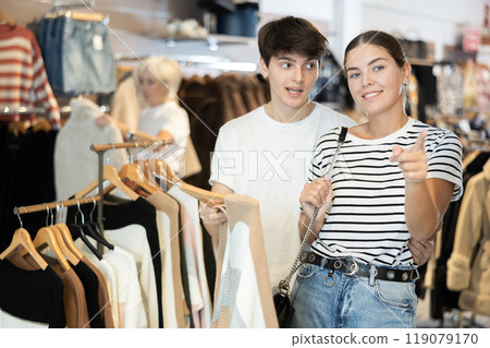 Young couple watching excitedly large stock of clothes in clothing store Young couple watching excitedly large stock of clothes in clothing store 119079170