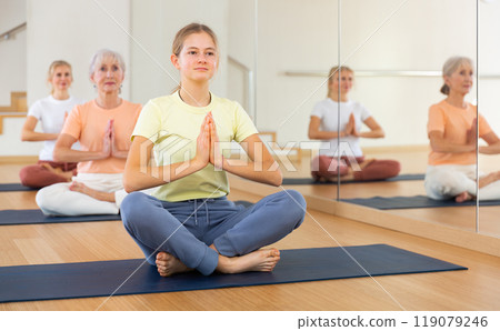 Teen girl with family in lotus position practices yoga in gym 119079246