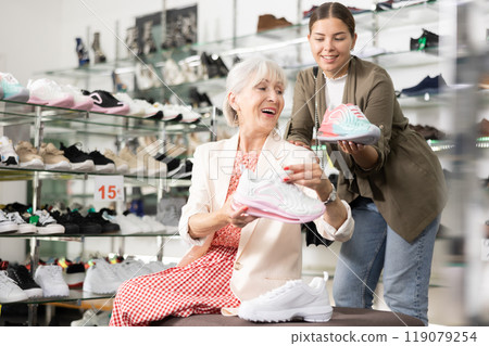 Elderly mom sits on bench and asks her daughter to advise fashionable sneakers for fitting Elderly mom sits on bench and asks her daughter to advise fashionable sneakers for fitting 119079254