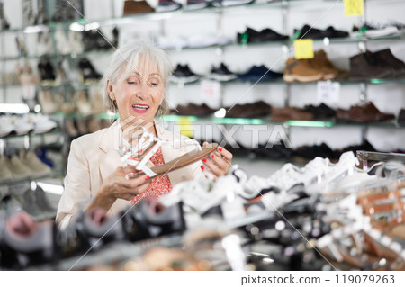 Elderly woman chooses sandals in shoe store Elderly woman chooses sandals in shoe store 119079263