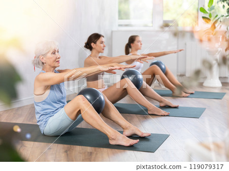 Family of three generations doing soft ball pilates exercises during group pilates class in studio 119079317