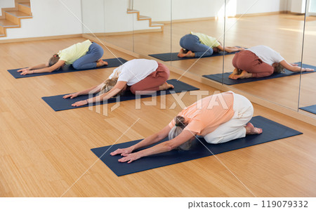 Various aged women kneeling in child's pose during group yoga training 119079332