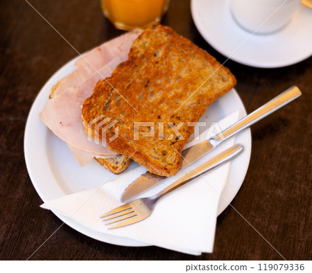 There is thin slice of soft and juicy ham between two slices of bread. 119079336