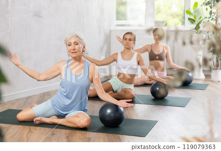 Family grandmother, mother and granddaughter perform fitness exercise sitting on floor with softball Family grandmother, mother and granddaughter perform fitness exercise sitting on floor with softball 119079363