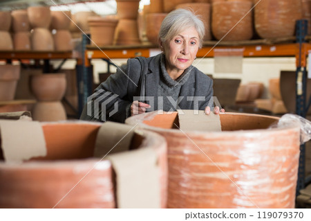 Aged woman selecting decorative earthenware pot in shop 119079370
