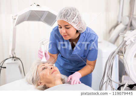 Old woman having face laser therapy procedure Old woman having face laser therapy procedure 119079445