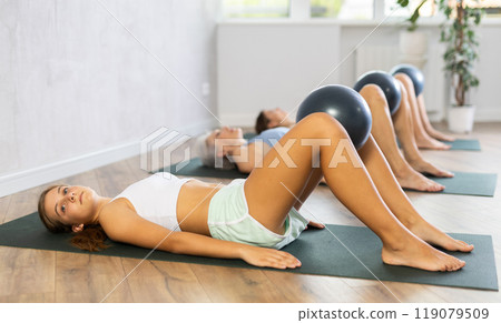 Fitness family in activewear working out with soft ball pilates on mat while doing upper body training in yoga studio 119079509