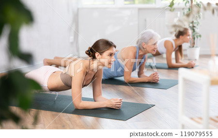 Three generations of women perform elbow plank Sampatasana in gym 119079555