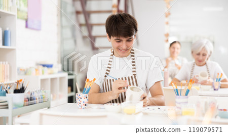 Cheerful skilled young artist painting ceramic cup in pottery workshop 119079571