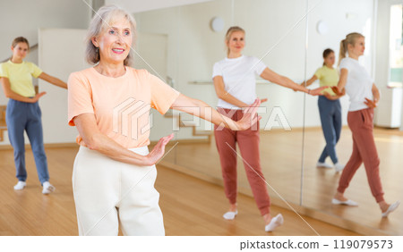 Positive woman doing aerobics exercises with group of people in dance center Positive woman doing aerobics exercises with group of people in dance center 119079573