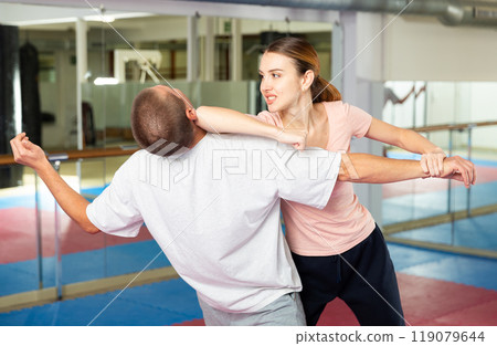Active girl conducts painful grip on self-defense training in gym Active girl conducts painful grip on self-defense training in gym 119079644