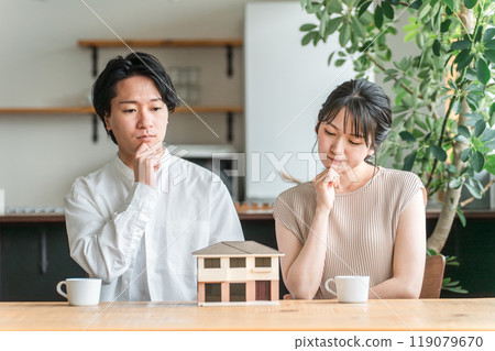 一對年輕夫婦正在查看房屋模型並考慮其房屋的平面圖（諮詢會議、房屋建築商、獨立式住宅） 119079670