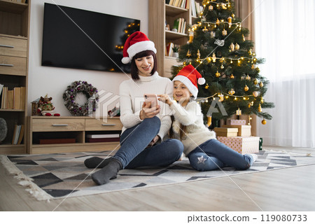 Mother and daughter enjoy festive moments by Christmas tree Mother and daughter enjoy festive moments by Christmas tree 119080733